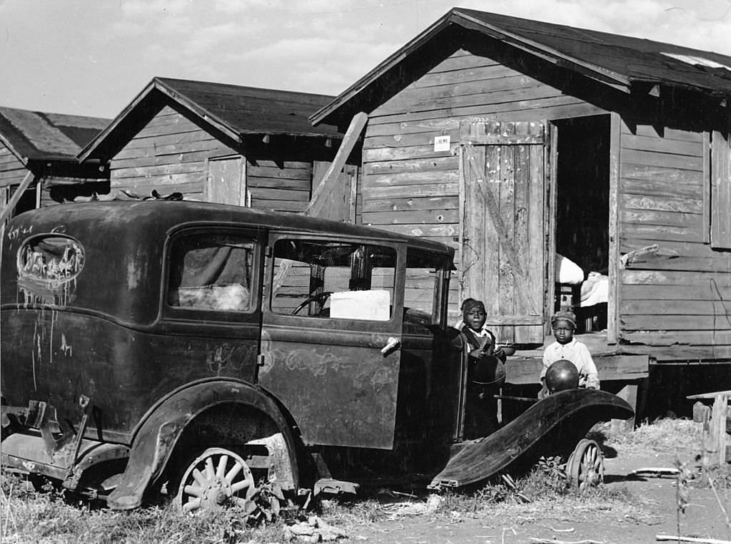 Children of migratory laborers stand outside their dilapidated houses, which were condemned by the Board of Health, but still used as living spaces, Belle Glade, Florida, 1941.