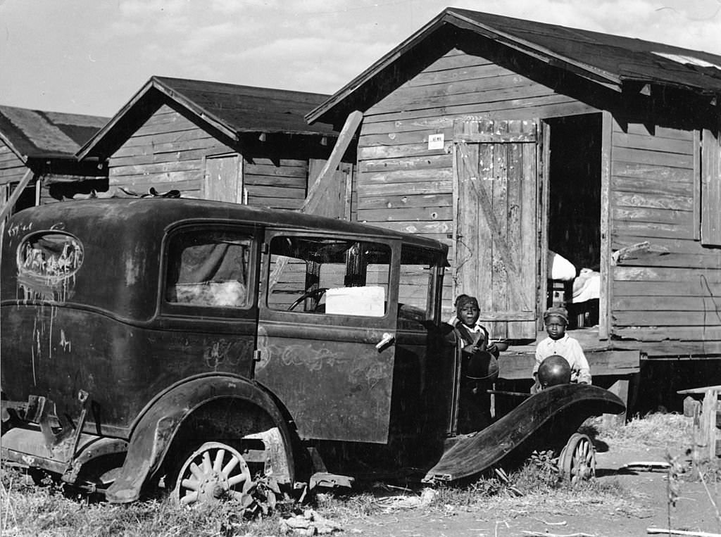 Children of migratory laborers stand outside their dilapidated houses, which were condemned by the Board of Health, but still used as living spaces, Belle Glade, Florida, 1941.