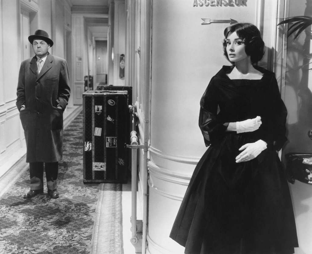 Ariane Chavasse (Audrey Hepburn) hides around a hallway corner from Monsieur X (John McGiver in a scene, 'Love in the Afternoon', 1957.