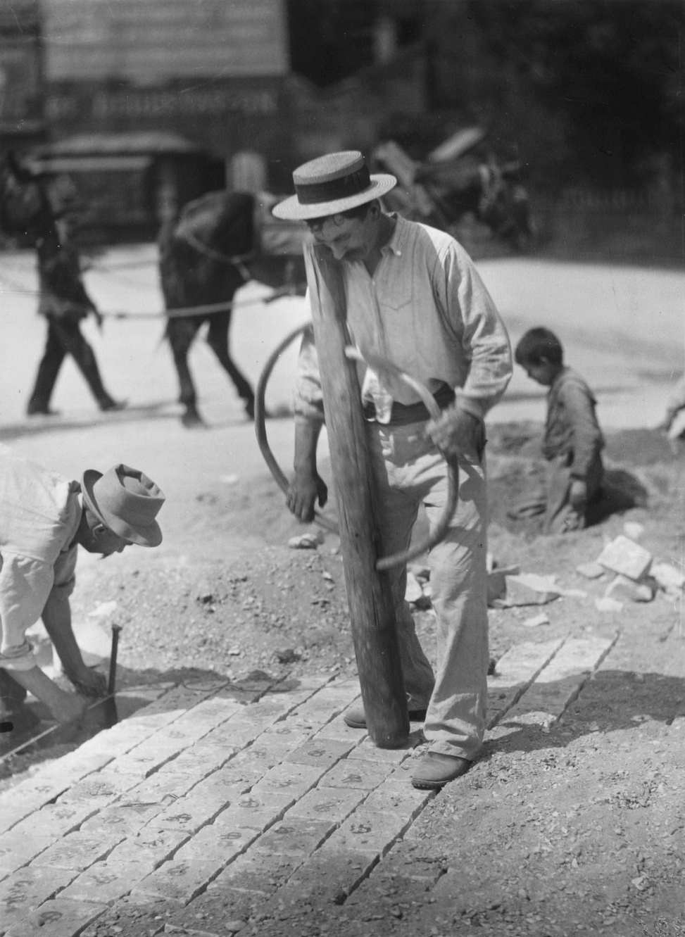 A man pounds paving stones on a street into an even surface, Paris, 1900