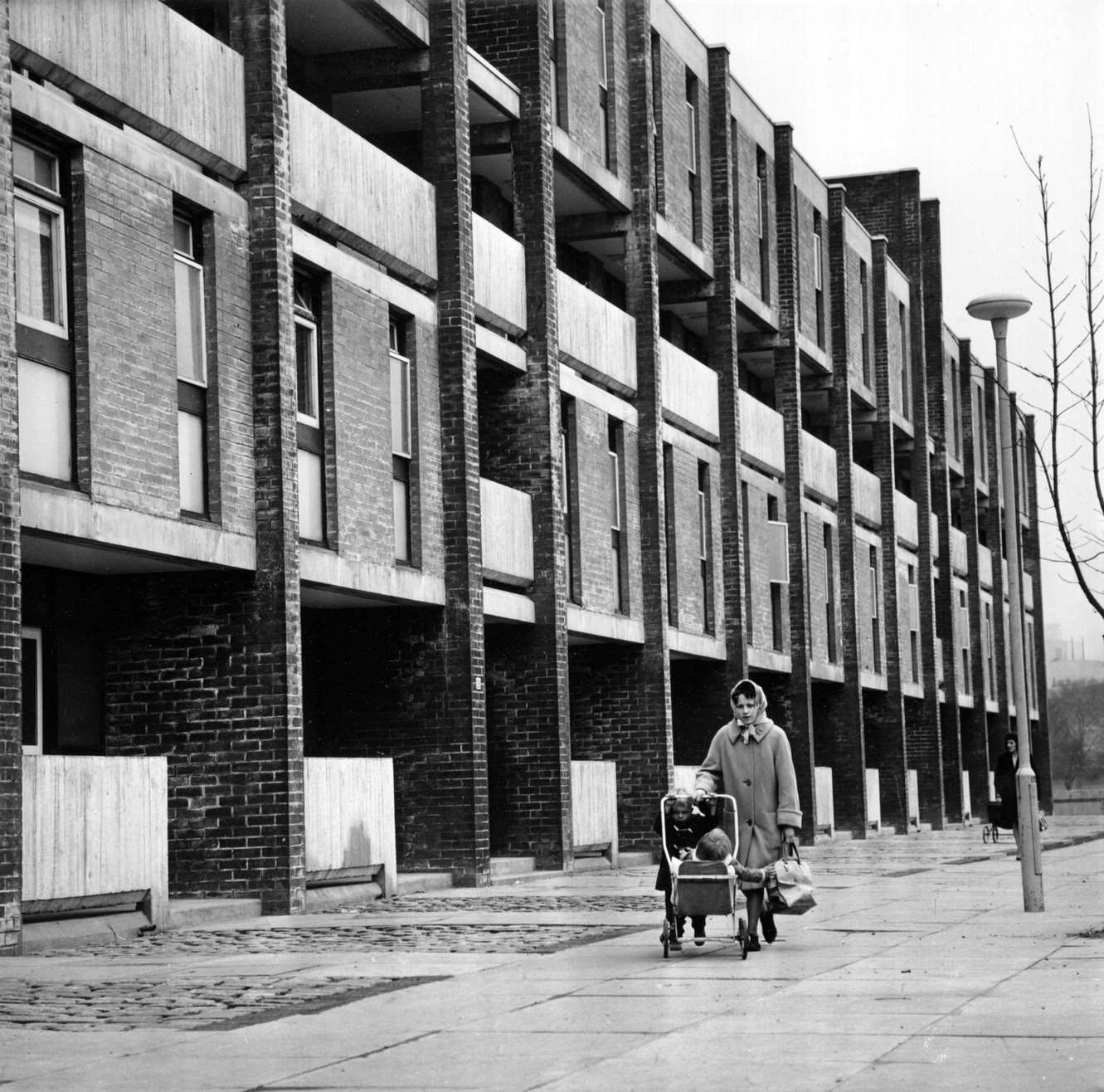 A woman walking past a block of modern housing with two young children in the Gorbals area of Glasgow, 1960