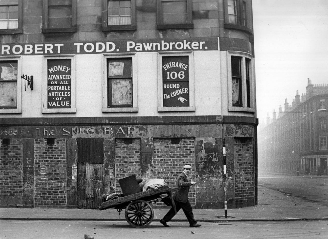 A man pulling a hand cart past a closed-down pawnbroker's shop in the Gorbals area of Glasgow, 1960