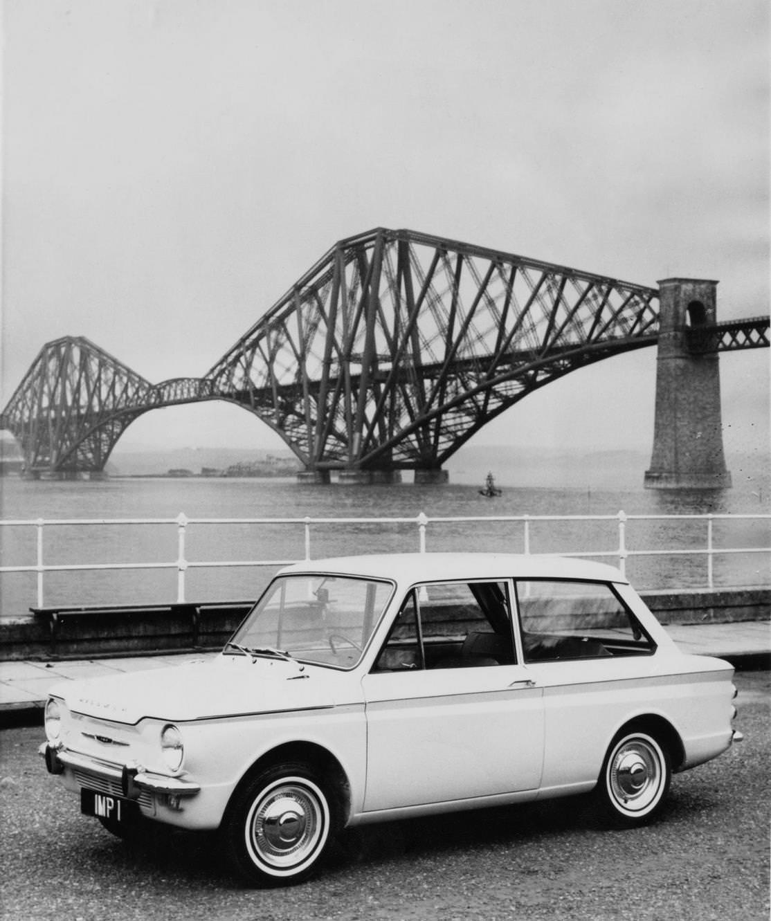 The Scottish built Rootes Group Hillman Imp compact, rear-engined saloon car seen near the Forth Bridge cantilever railway bridge across the Firth of Forth on 3 May 1963 near Edinburgh, Scotland.