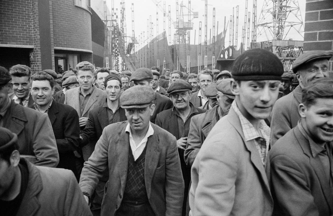 A group of workers leave a shipyard at clocking off time in Greenock, Renfrewshire, Scotland, 1963.