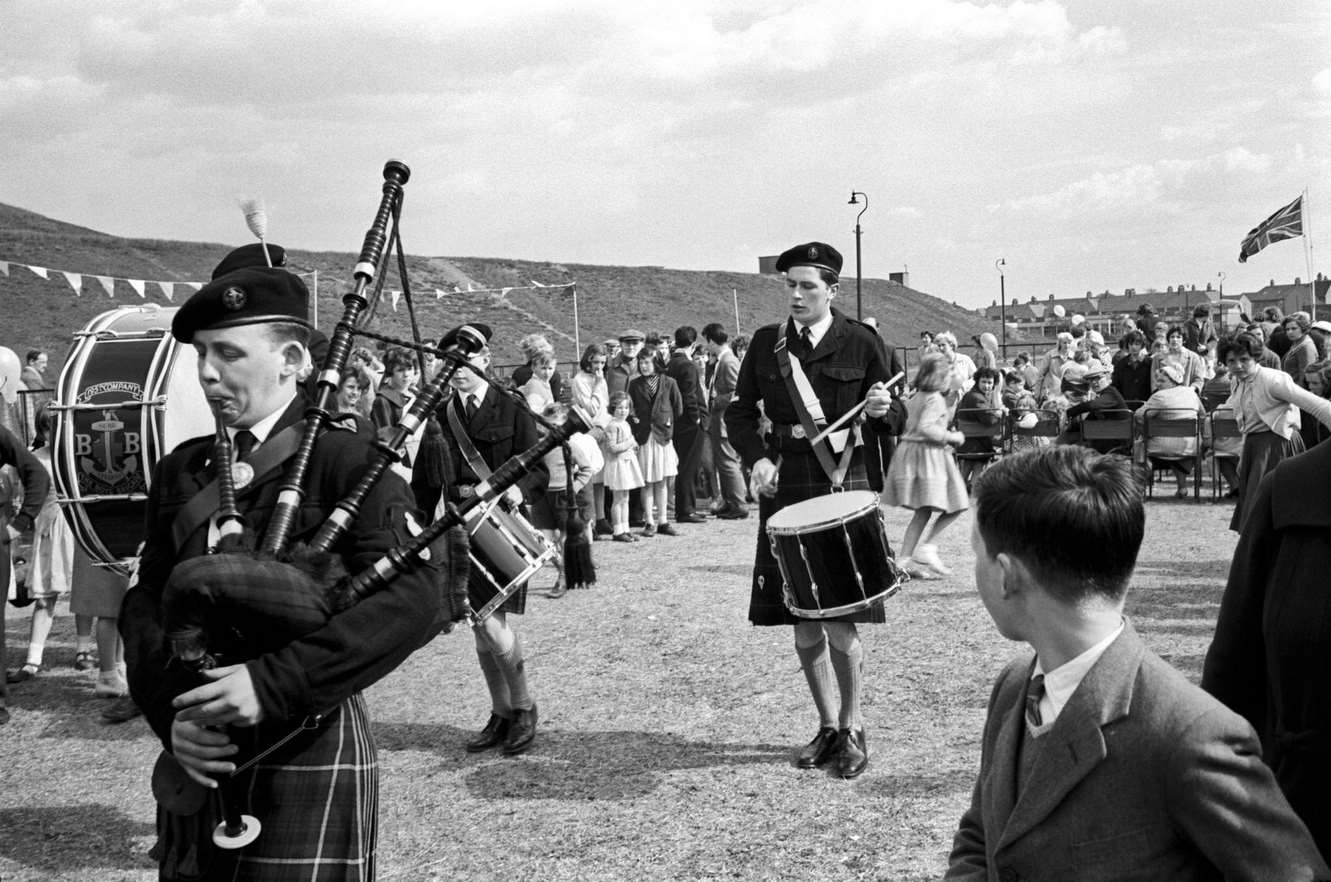 A village festival, with the band; in a close-up, there is a bagpipe player, who wears the kilt, and on the background is a crowd, Scotland, 1968