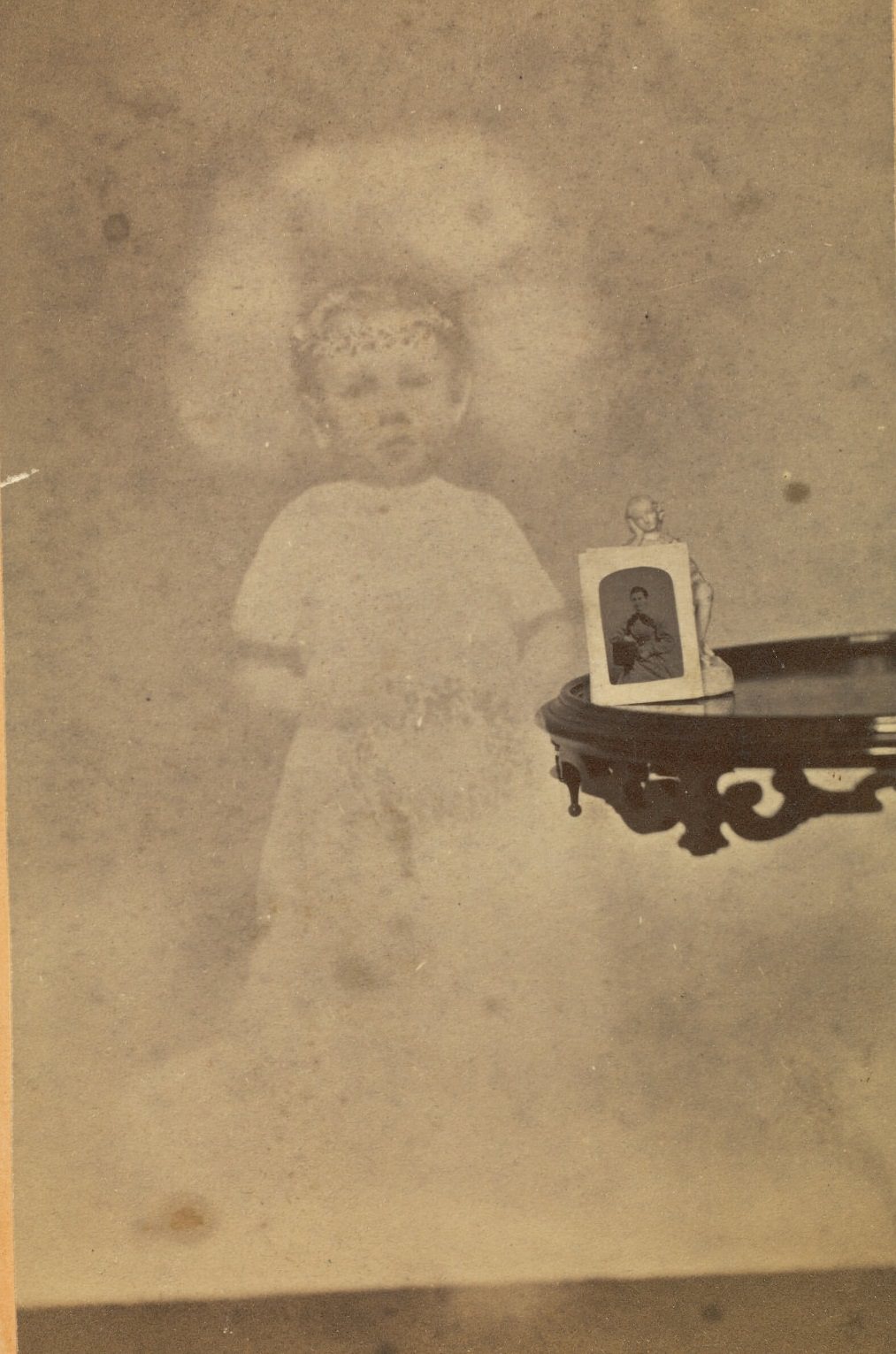 Small statuette and photograph on a side table, with the faint image of a young boy floating next to it.