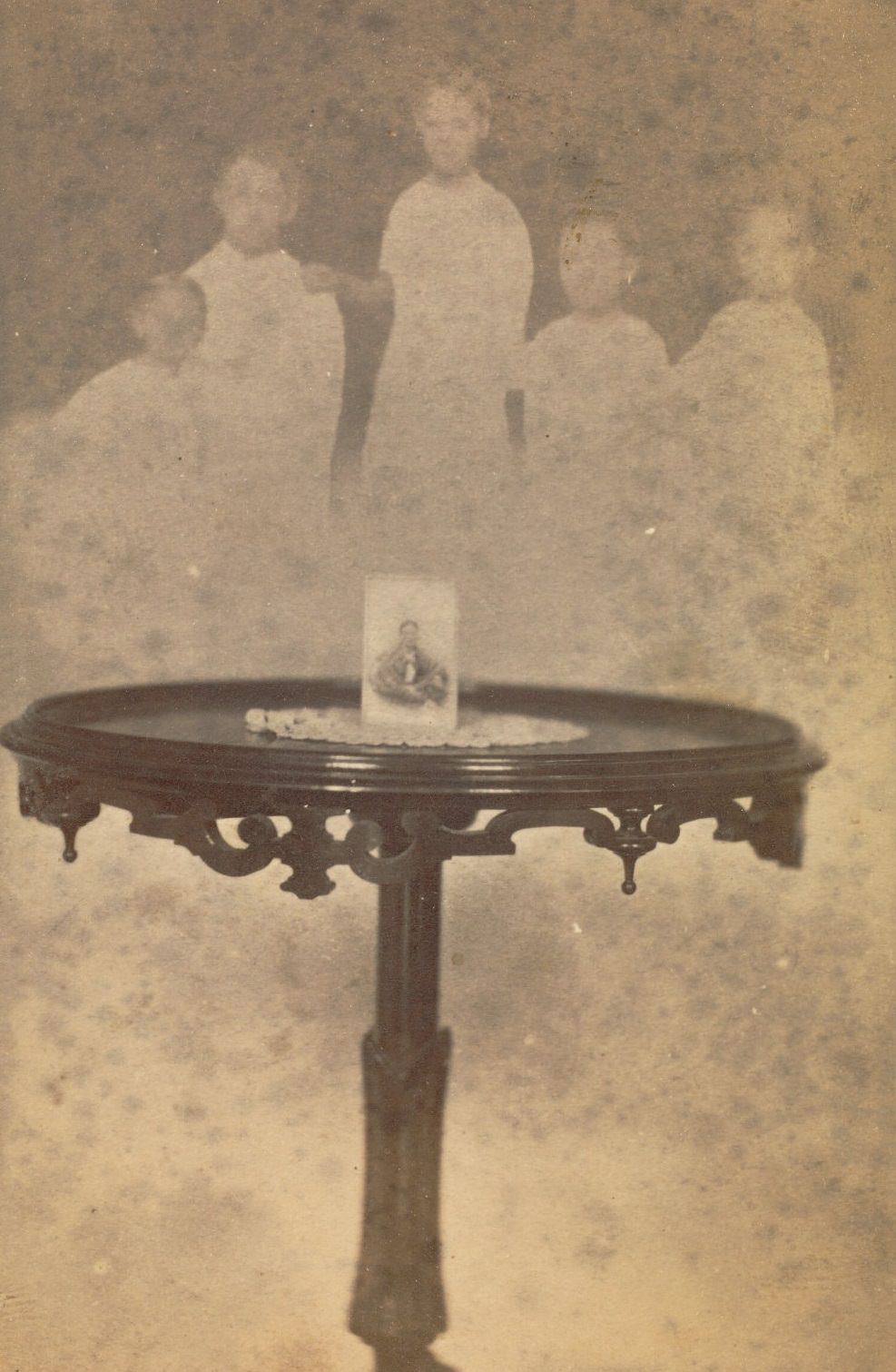 Small round table with a portrait sitting atop it, with the faint image of a group of five people, a man and four children, floating above it
