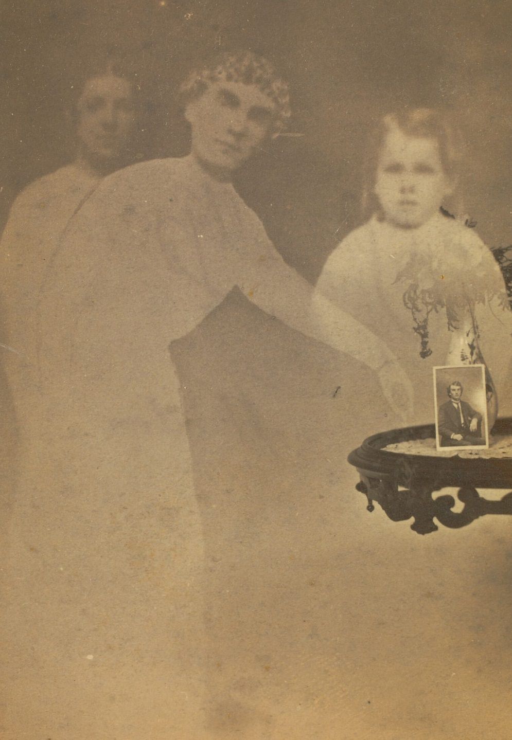 A small photograph propped against a vase of flowers on a side table. Faint images of a woman and two children are visible next to the table.
