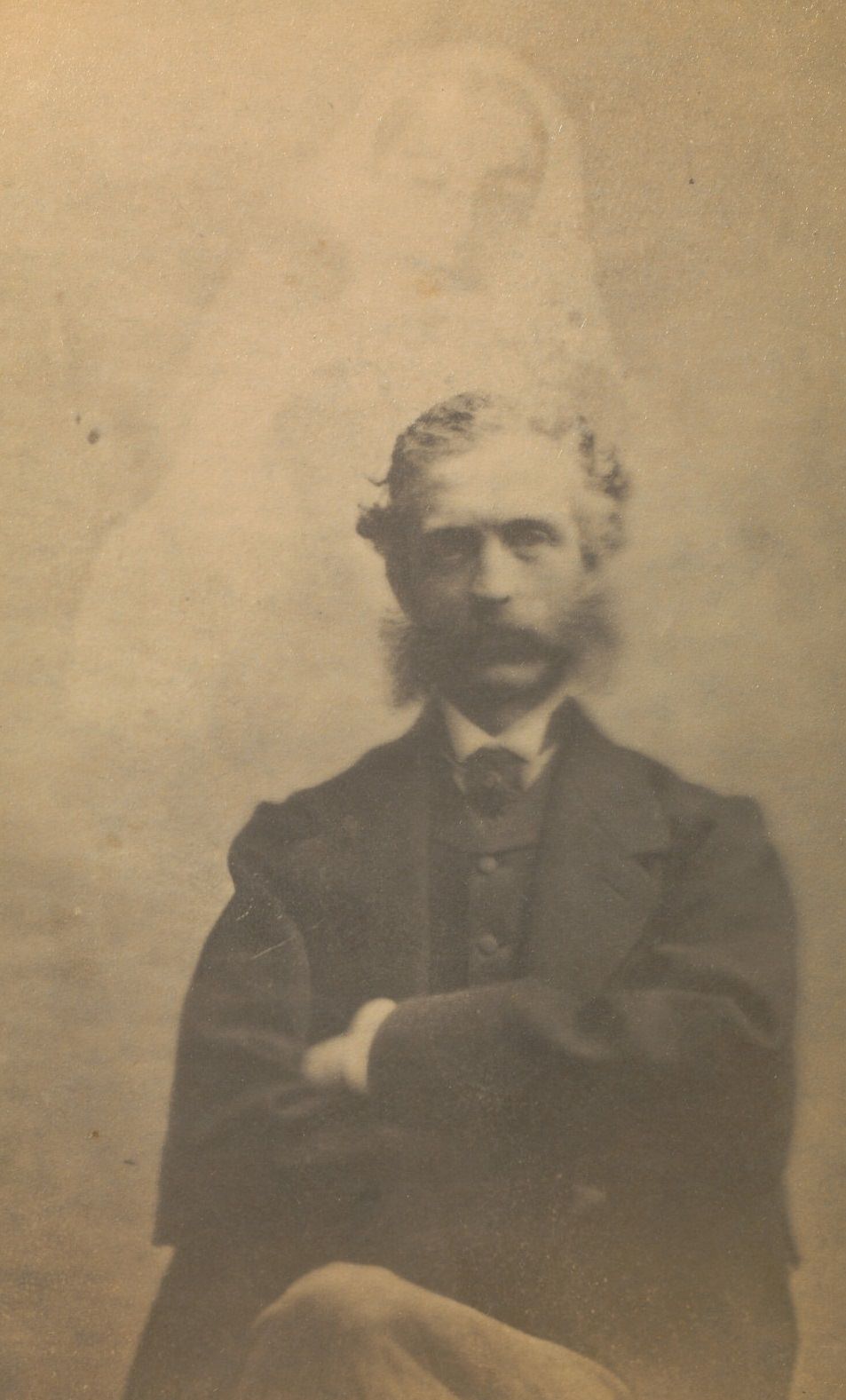 Portrait of a seated man, facing the camera with his arms folded across his chest.