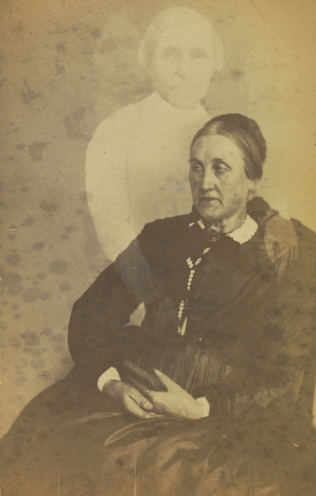 Portrait of a seated elderly woman, holding a book in her lap. Faint images of a woman and two men are visible above her.