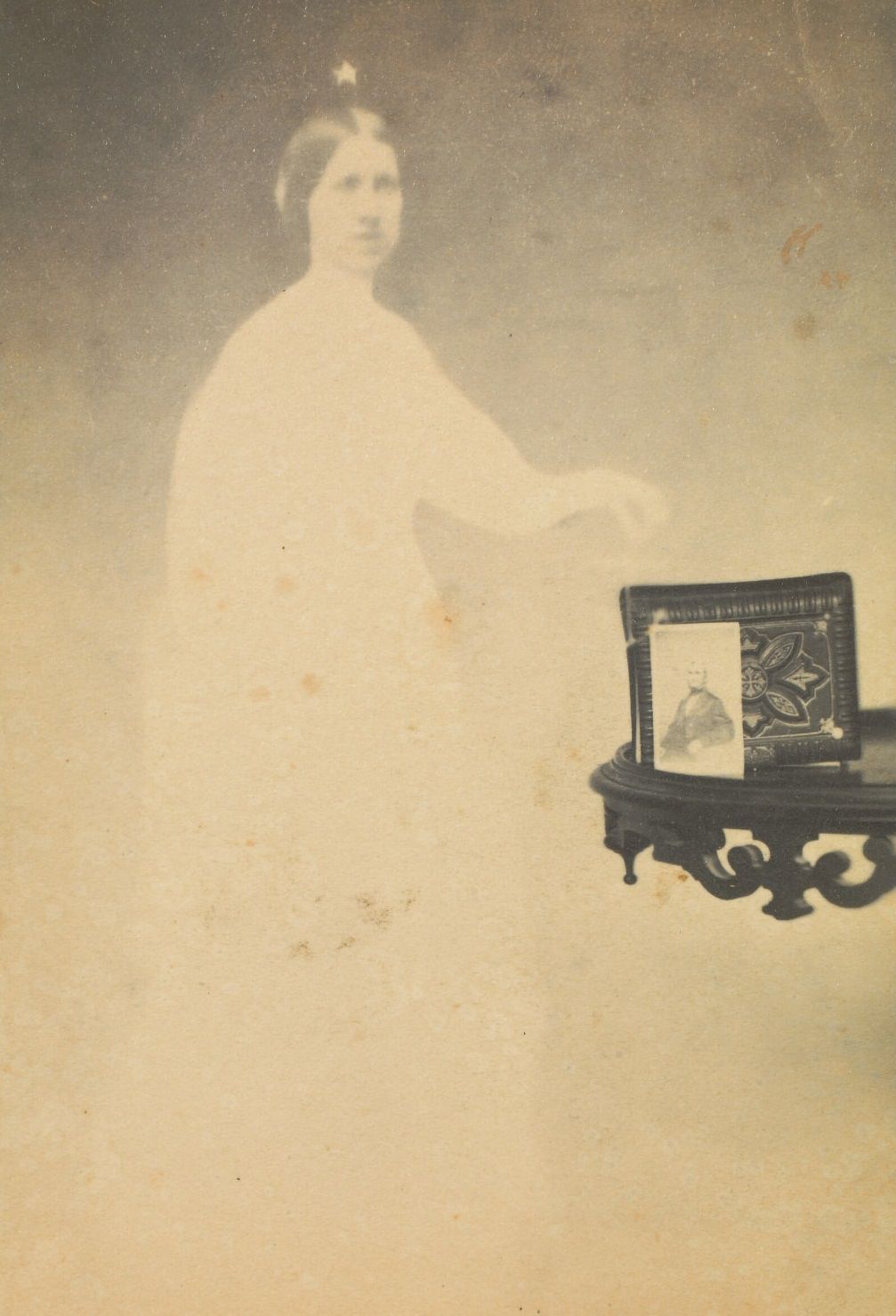 A photograph propped against an album on a side table, with the faint image of a woman next to it.