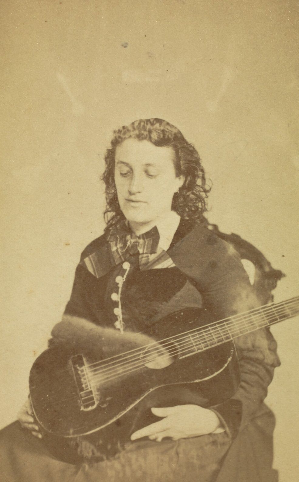 Portrait of a seated woman holding a guitar in her lap. A very, very faint image of a person is behind her.