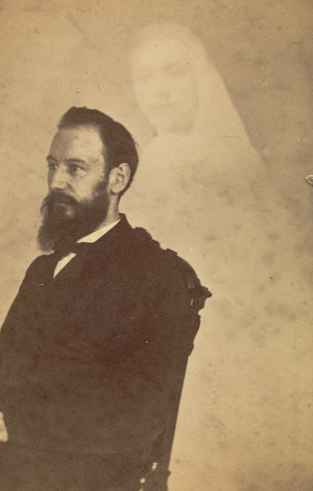 Profile portrait of a seated man with a beard. A faint image of a woman is visible behind him.