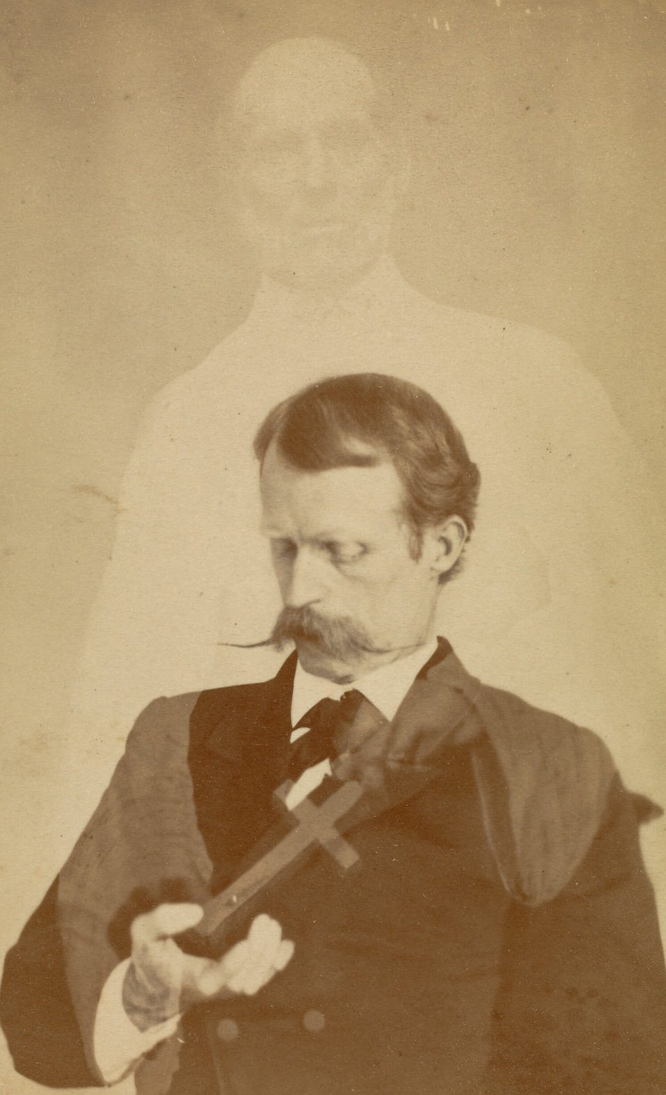 Portrait of Harry Gordon looking down into his hand, while the faint figure of a bearded man appears behind him, with hands that seem to be placing a crucifix into the open hand of the sitter.