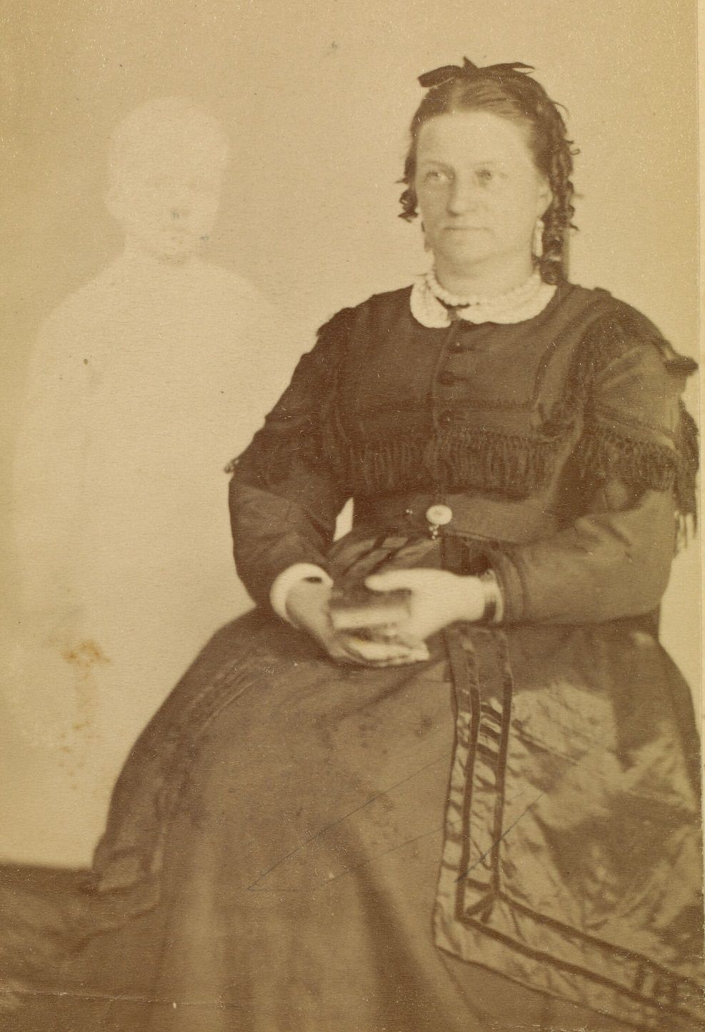 Portrait of Mrs. French, wearing a dark dress, holding a book in her lap. The faint image of a boy appears beside her.
