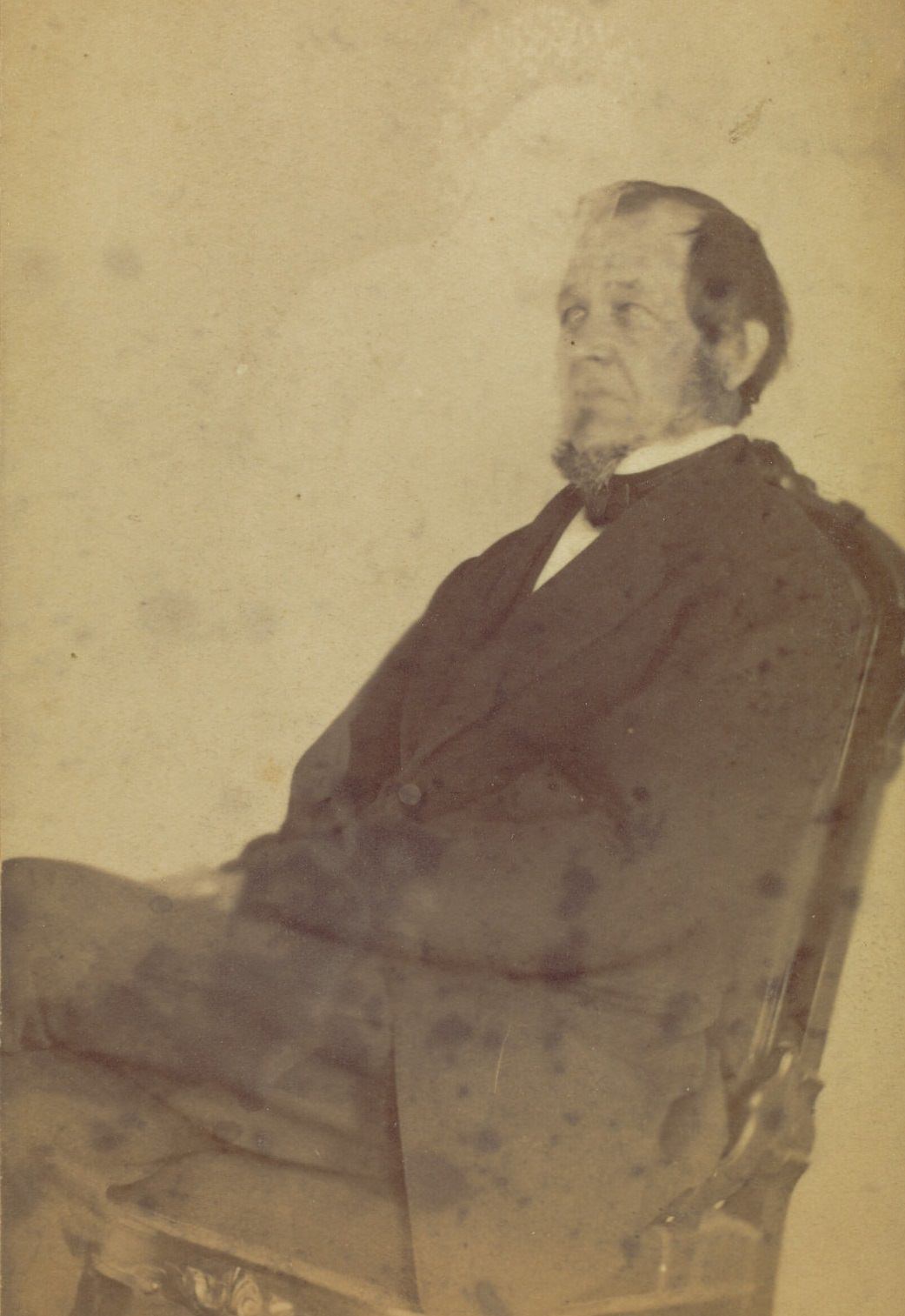 Profile portrait of a seated man with a goatee. A very faint image of a woman is visible above him.