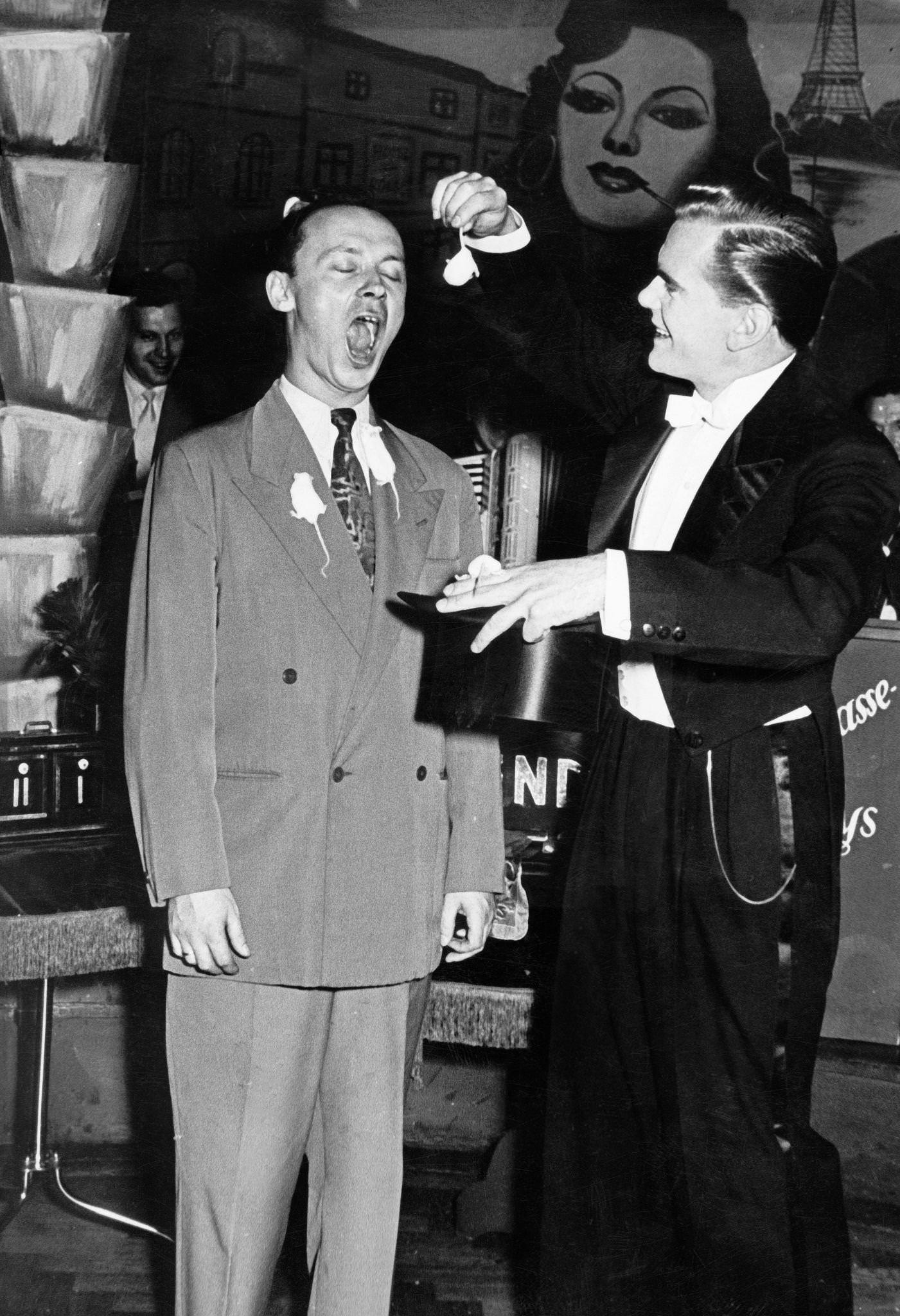 A magician in a nightclub on the Reeperbahn in Hamburg tempts a spectator to eat a goldfish, 1950s.