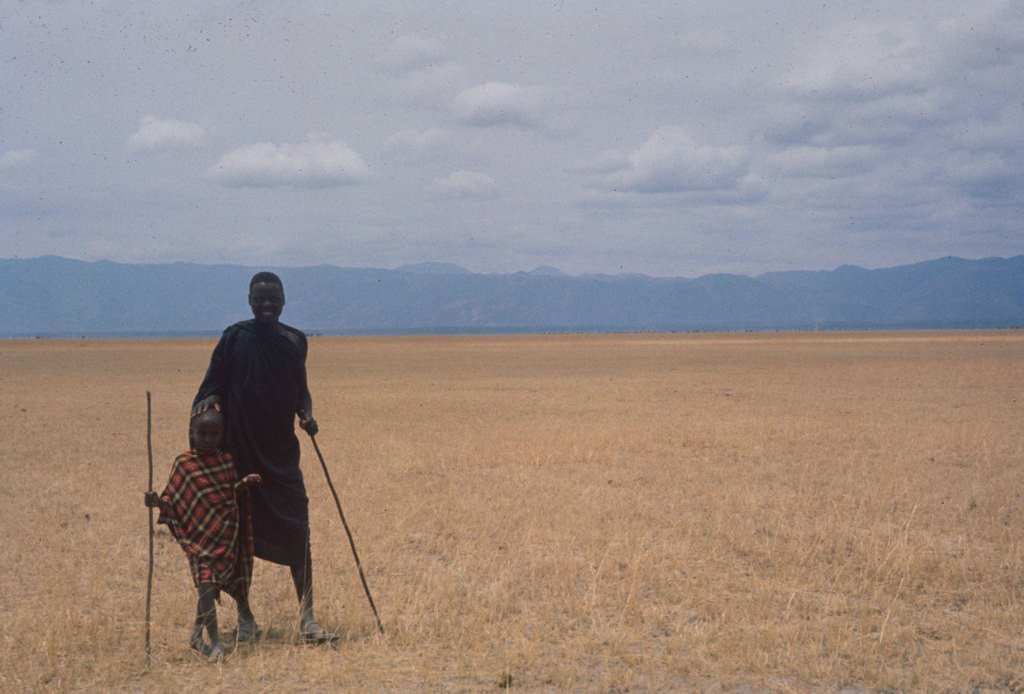 A man and his son as they smile and stand in an open field, Tanzania, 1962.