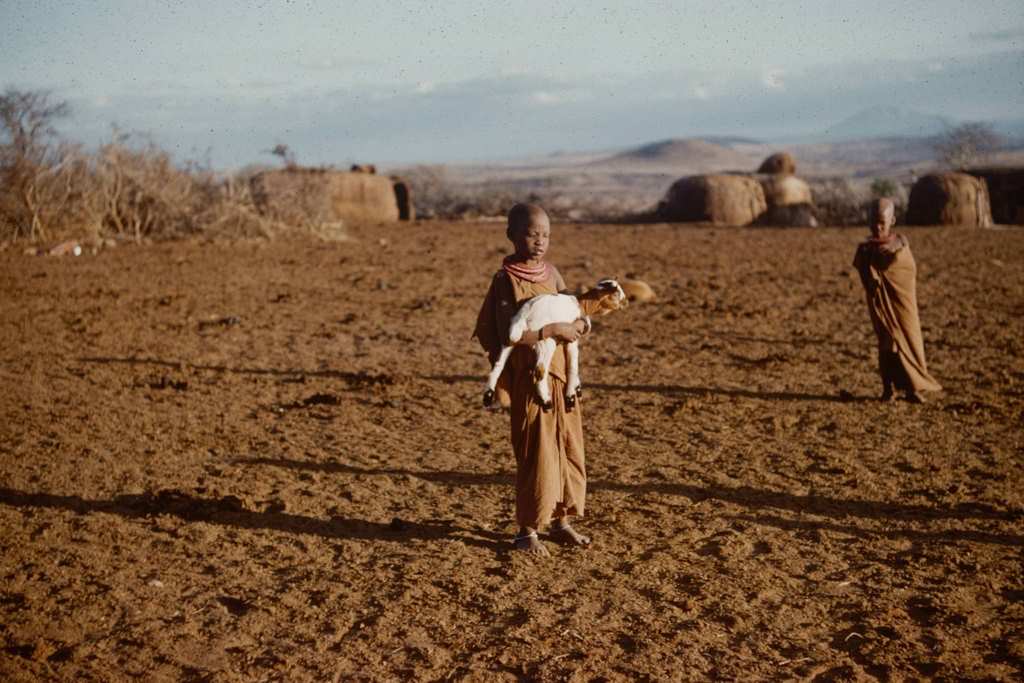 A young boy as he holds a goat kid in his arms in a small village, Tanzania, 1962.