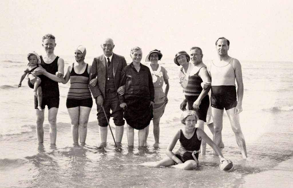 Two ladies on holiday in beach chairs at the seaside, with a family playing behind, in Scheveningen near The Hague, 1925