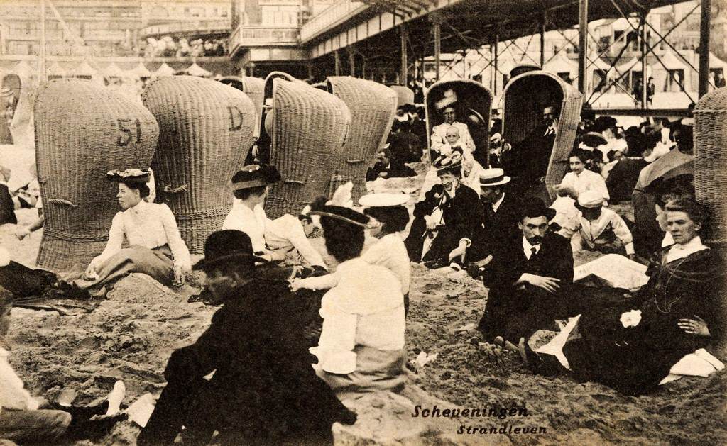Holidaymakers sitting on the sand and in beach chairs at the seaside in Scheveningen near The Hague in the Netherlands, 1908.