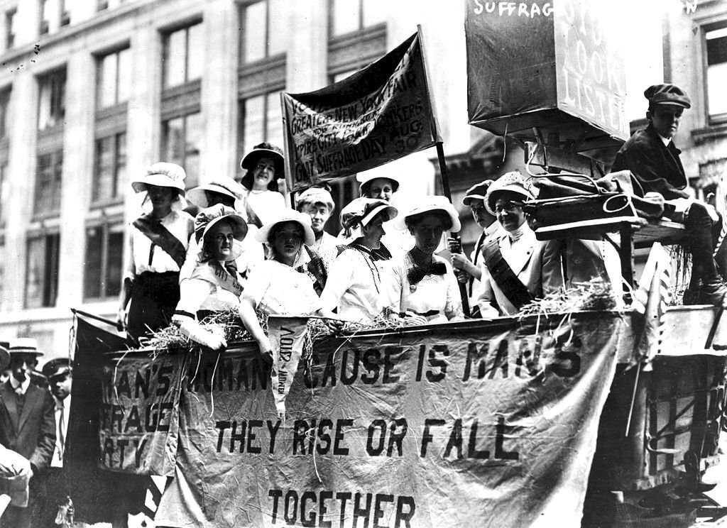 Women riding in a Hay Wagon float in a suffrage parade, 1913. A banner hanging upon the float quotes Tennyson's phrase 'The Woman's Cause Is Man's; They Rise Or Fall Together'.