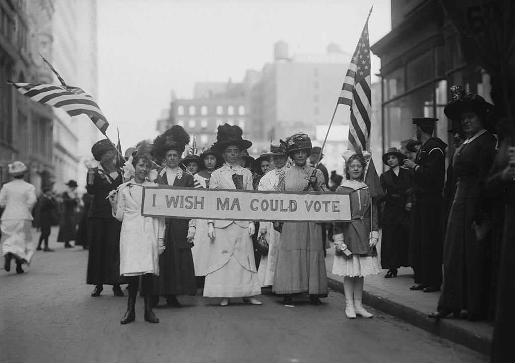 A group of Women's Suffrage activists march in a parade carrying a banner reading 'I Wish Ma Could Vote' circa 1913.