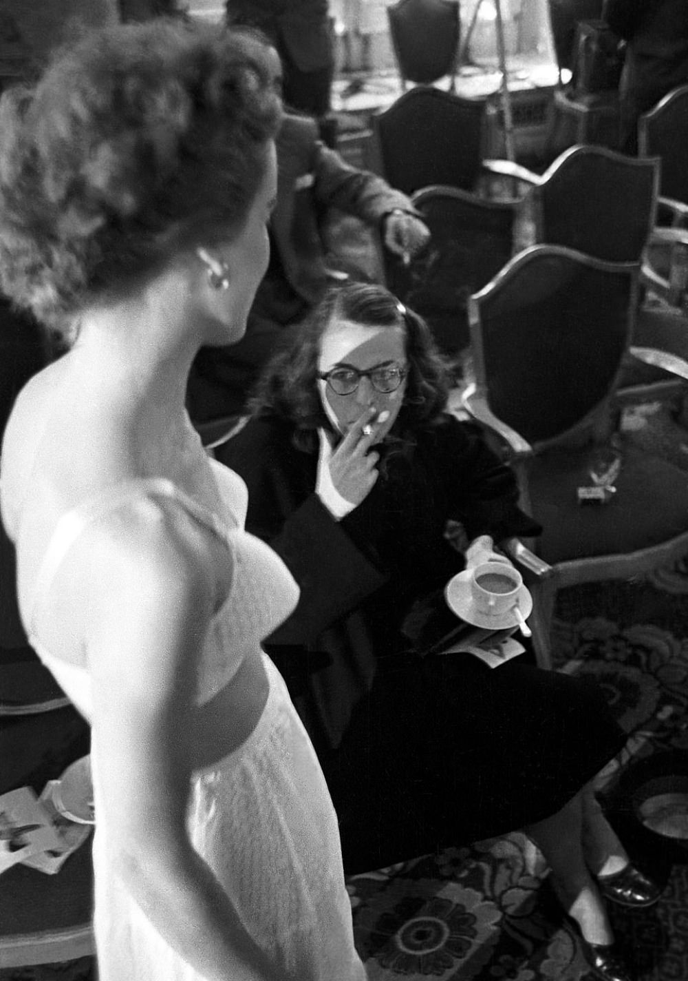 A woman smoking a cigarette, right, inspects the innovative bra on a model as she walks the catwalk.