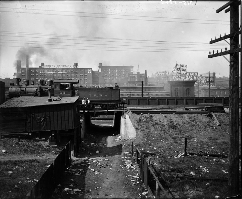 Terminal Railroad Association train engine with tender stopped in rail yard, warehouses in the Cupples station block are visible in the background, 1909