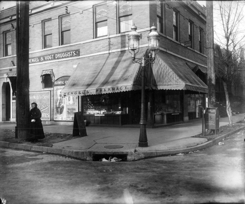 Mengel & Vogt pharmacy at Taylor and Page Avenues, 1906. A woman is standing next to a pole in front of the building. The building still exists and appears to be vacant.