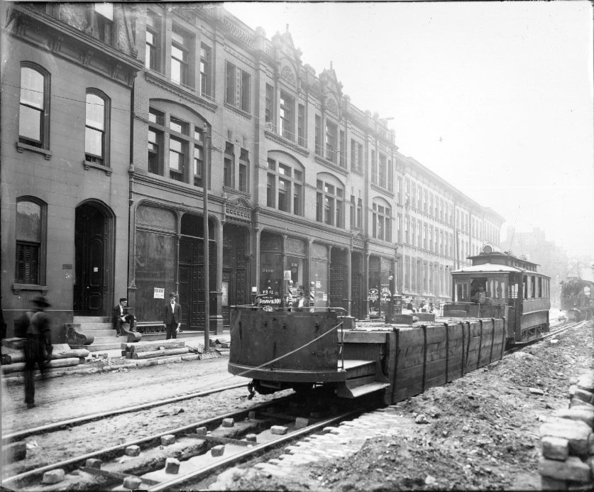 Streetcars on street under repair, 1909 .A modified streetcar with the cab removed is in the foreground. Men are visible in the background on the sidewalk in front of the businesses.