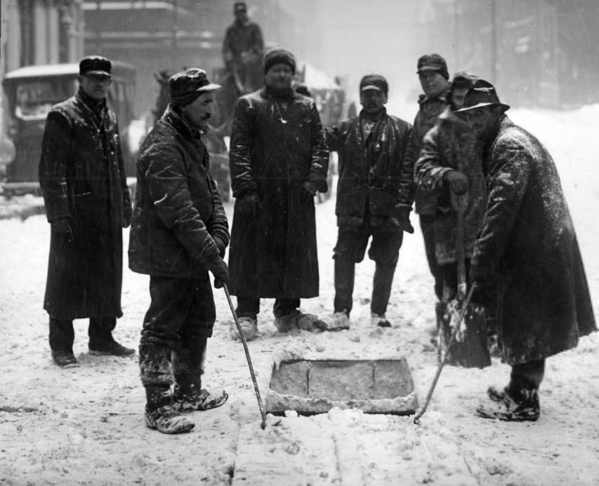 Team of men working in the middle of a city street during a snowstorm, 1902