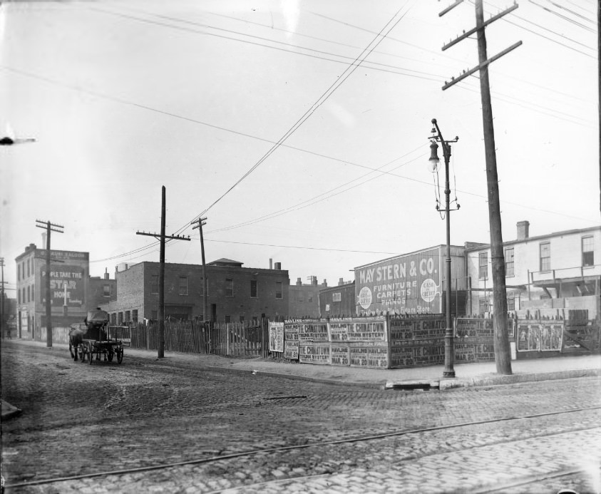 City street intersection with theater posters and building billboards visible, 1907