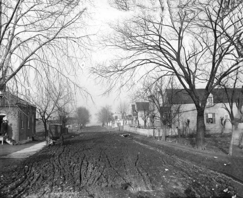 Unpaved road that is muddy, many ruts from carriage wheels are visible, 1902