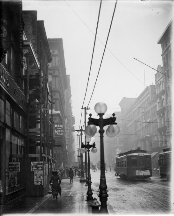 Rainy city street with street lamps visible in the foreground, 1901