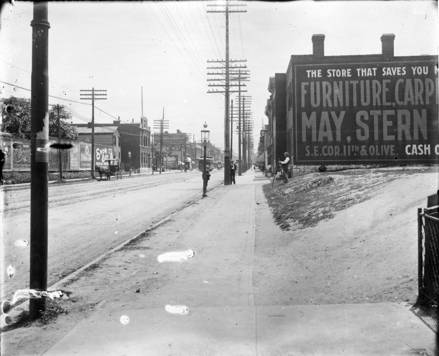 Looking along city sidewalk with major street on one side and vacant lot on the other, 1906