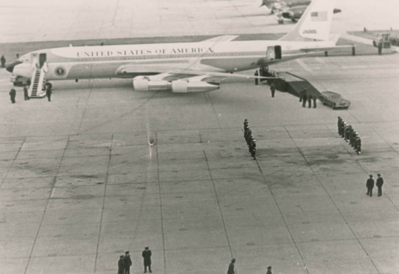 Air Force One carrying the casket of President Lyndon B. Johnson. People stand on the tarmac, some at attention, 1973