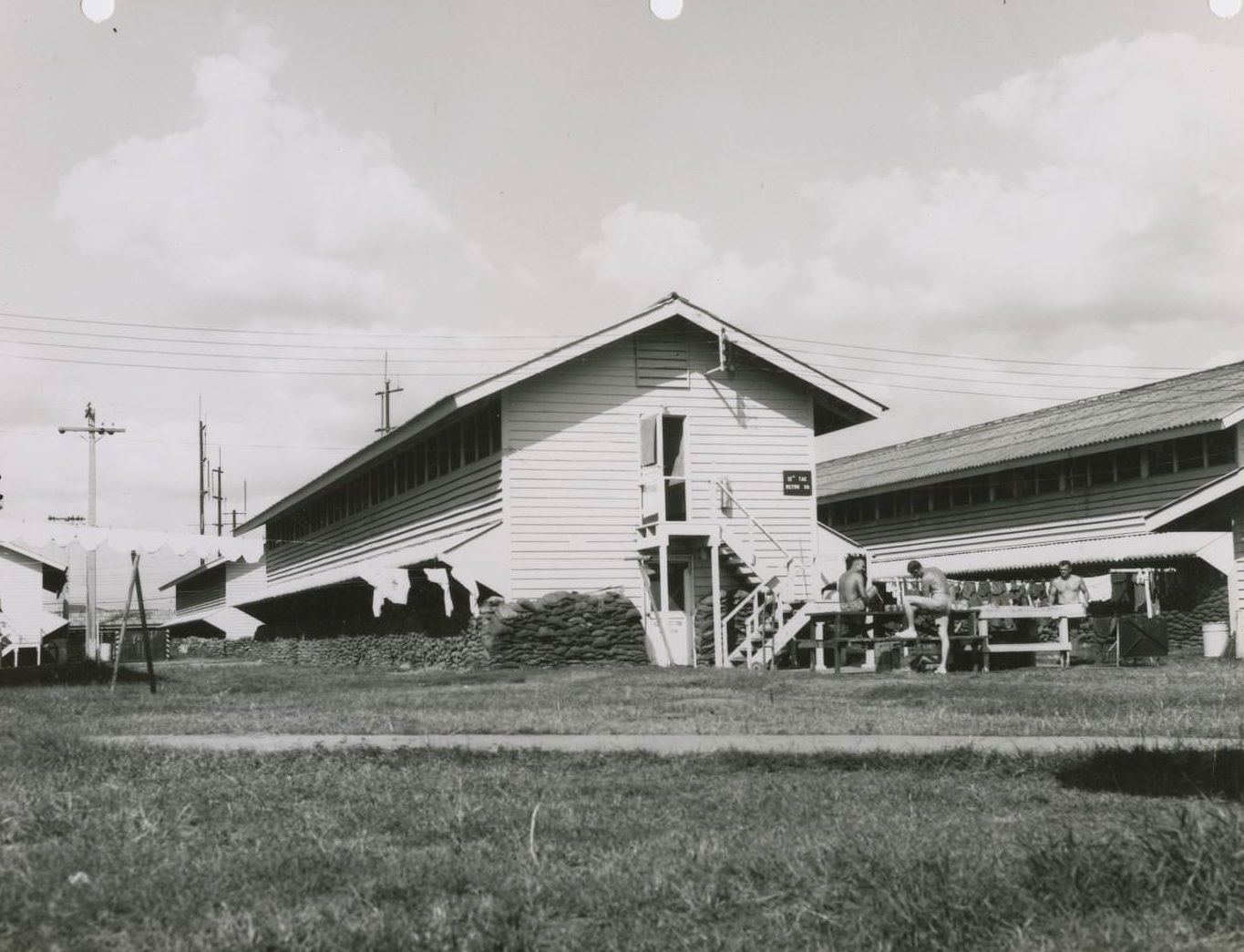 Old Men's Barracks at the Bergstrom Air Force Base, 1970. There is a line of laundry between houses to the left, and men sit at a picnic table to the right.