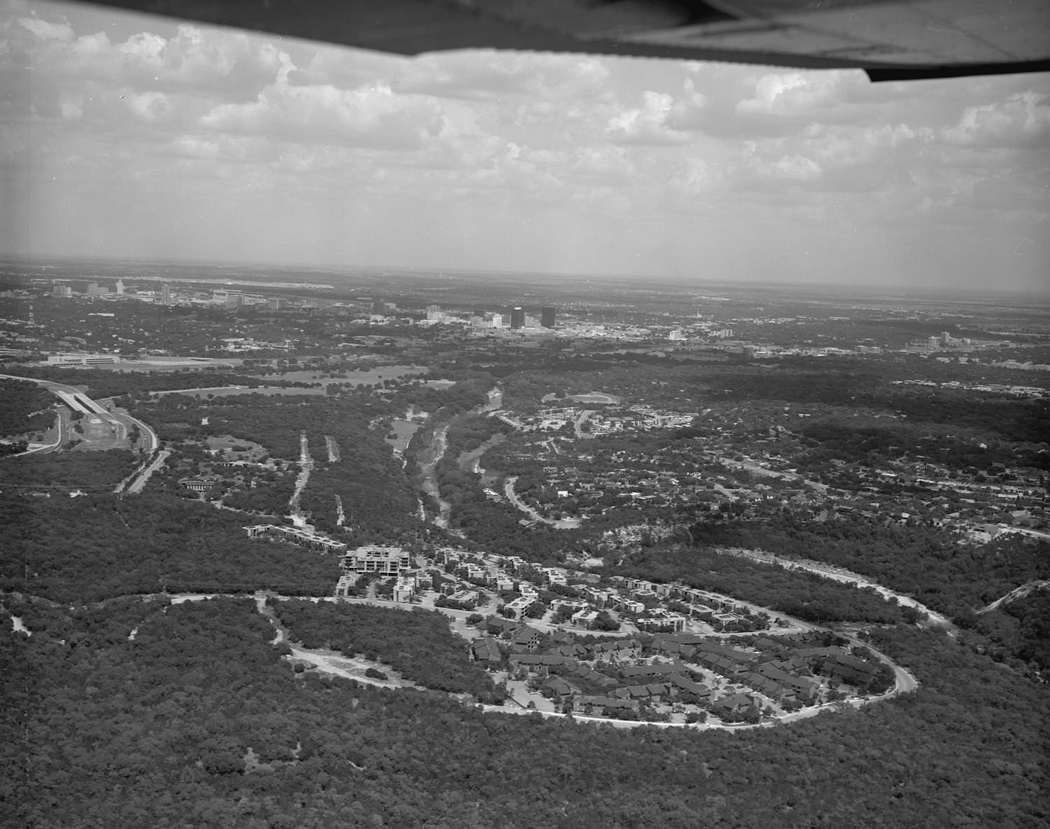 The sky of downtown Austin and the new Austin high school building where the city can be seen in the distance, along with small neighborhoods and suburbs in the foreground, 1978