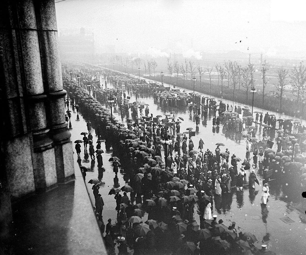 The suffrage parade, with spectators looking on in the rain, on South Michigan Avenue across from Grant Park in the Loop community area of Chicago, Illinois, 1910s.