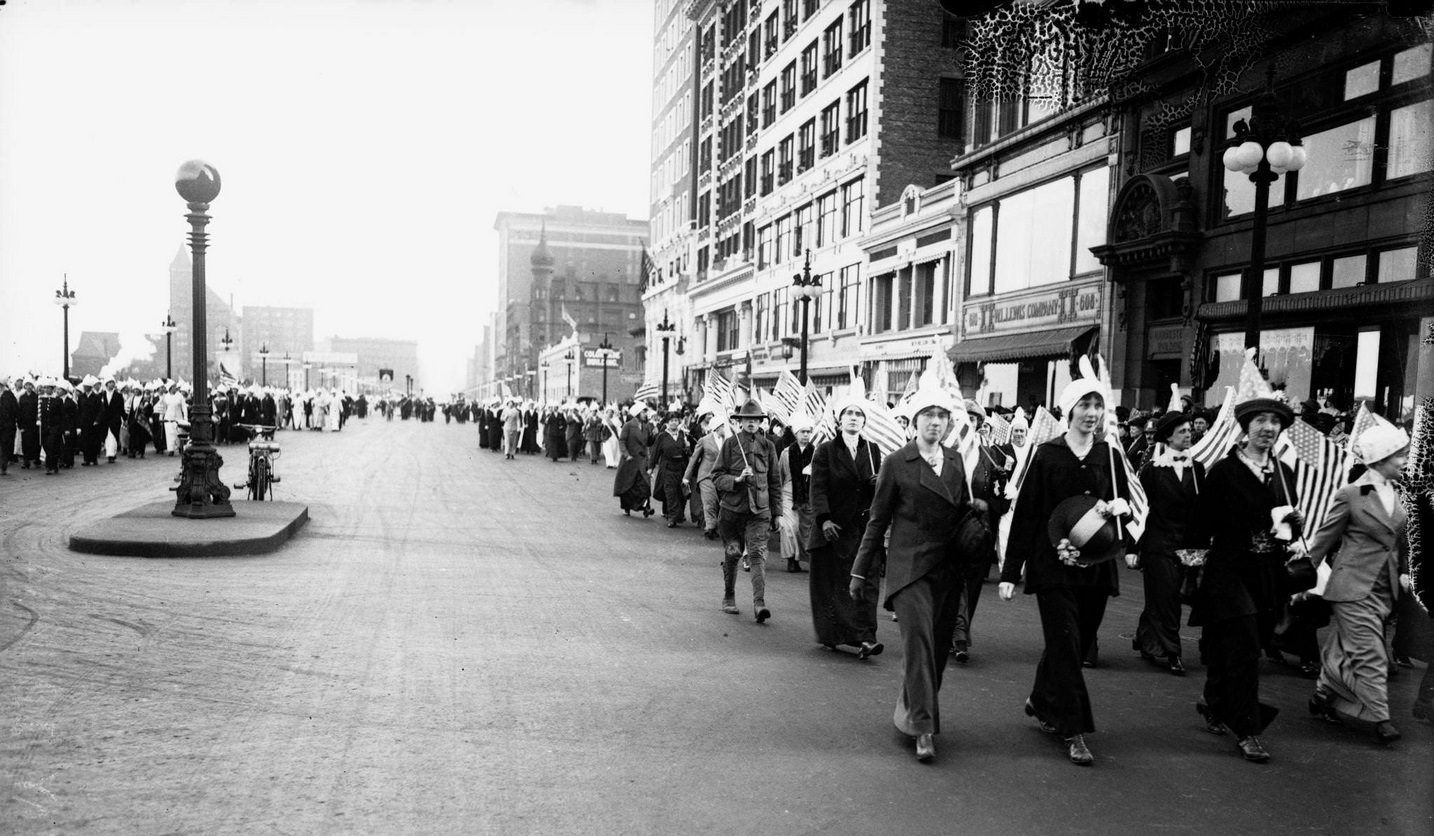 Women wearing parade hats and marching in parade formation north on South Michigan Avenue with another group of women marching on the east side visible in the background in the Loop community area, Chicago, Illinois, May 2, 1914.