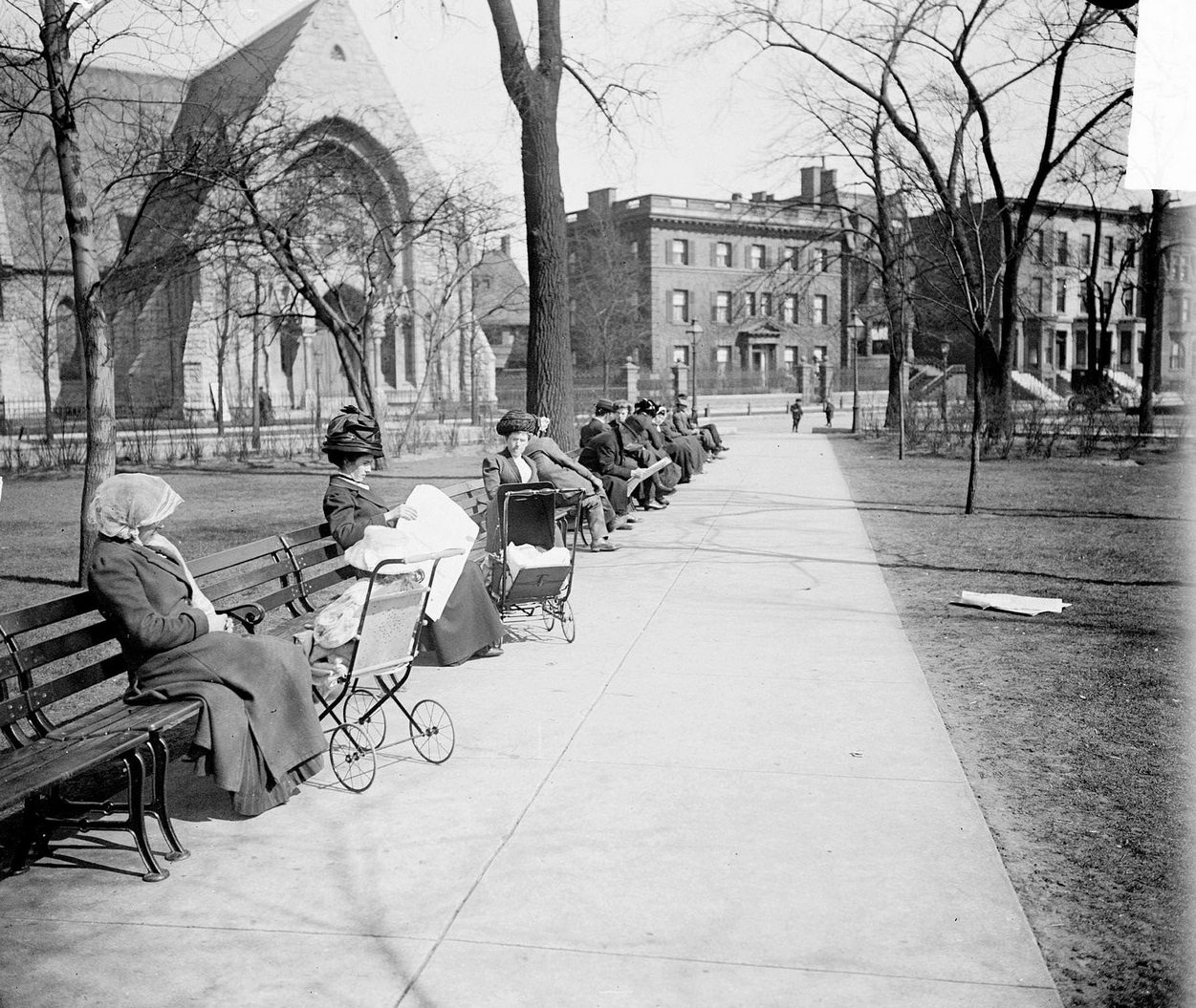 People sitting on benches along a pathway through Washington Square Park in Spring in the Near North Side community area, Chicago, Illinois, 1910s.