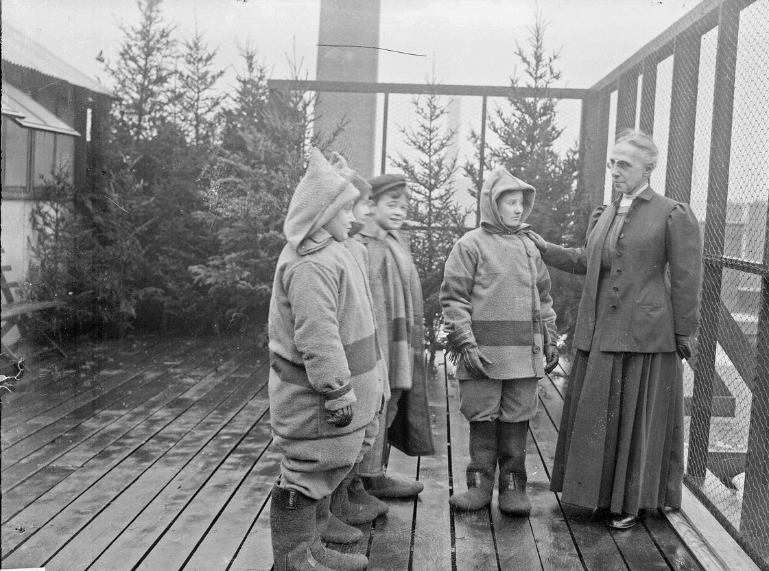 Superintendent of schools Mrs Ella Flagg Young standing with students outdoors at the Mary Crane Nursery, an open-air school, located at 782 West Cabrini Street (formerly 782 Ewing), Chicago, Illinois, 1910s.