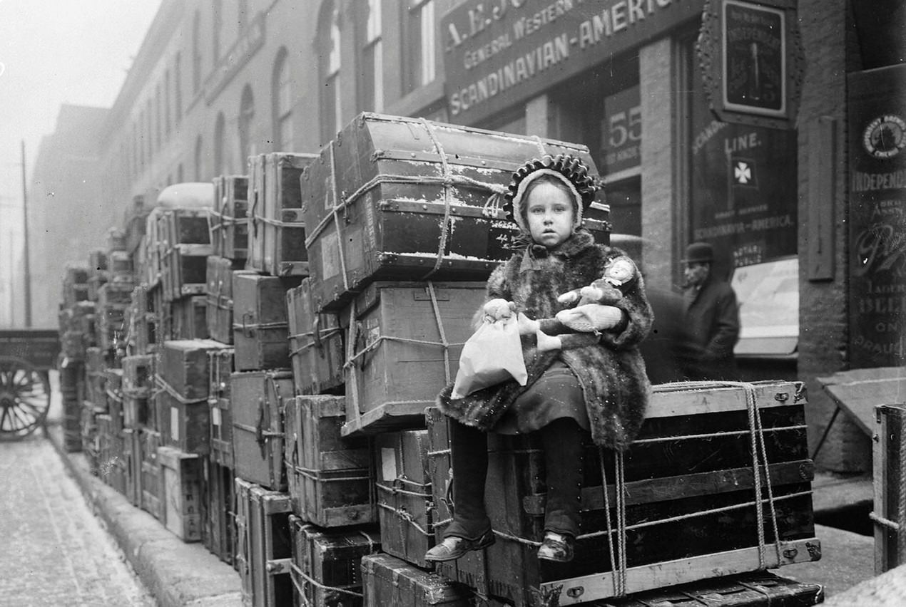 Girl sitting on stacked trunks belonging to Norwegians going home to Norway, Chicago, Illinois, 1910s.