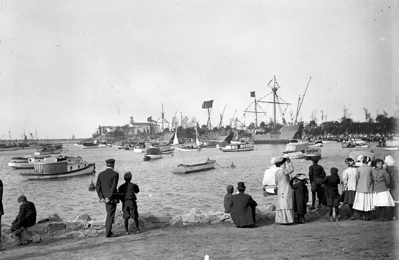 People standing in Jackson Park on the shore of Lake Michigan looking at caravels in the harbor near the La Rabida, Chicago, Illinois, 1910s.