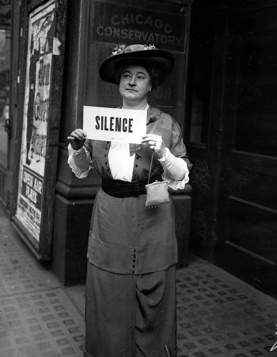 Mrs CL Hartwell holding a sign that reads, Silence, standing in front of the Chicago Conservatory in Chicago, Illinois, 1910s.