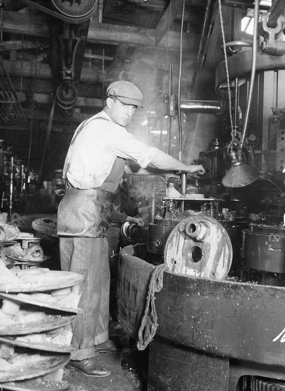 Baseball player Jim Vaughn, of the National League's Chicago Cubs, wearing street clothes and holding on to a lever attached to a large piece of machinery, standing in a room filled with machinery in or near Chicago, Illinois, 1918.