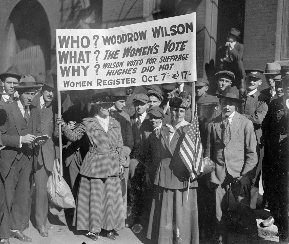Mrs George Taylor and Mrs Catherine Waugh McCulloch, holding a banner and surrounded by men, standing in front of the LaSalle Street Station, Chicago, Illinois, 1910s.