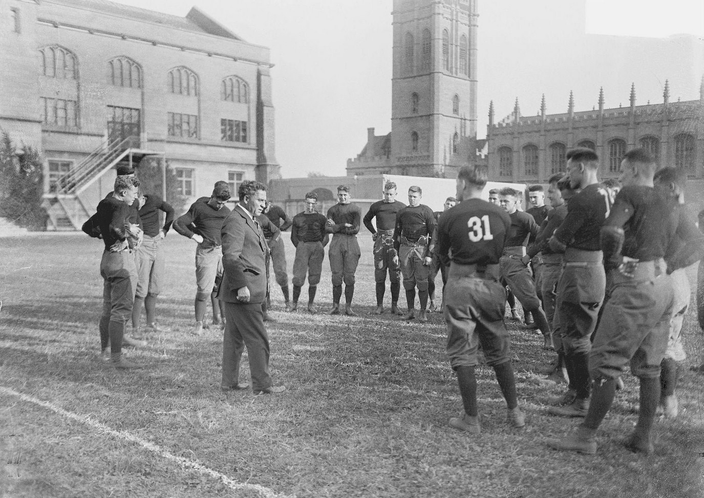University of Chicago football team players standing around Coach Alonzo A Stagg on an athletic field at the university campus, Chicago, Illinois, 1916.