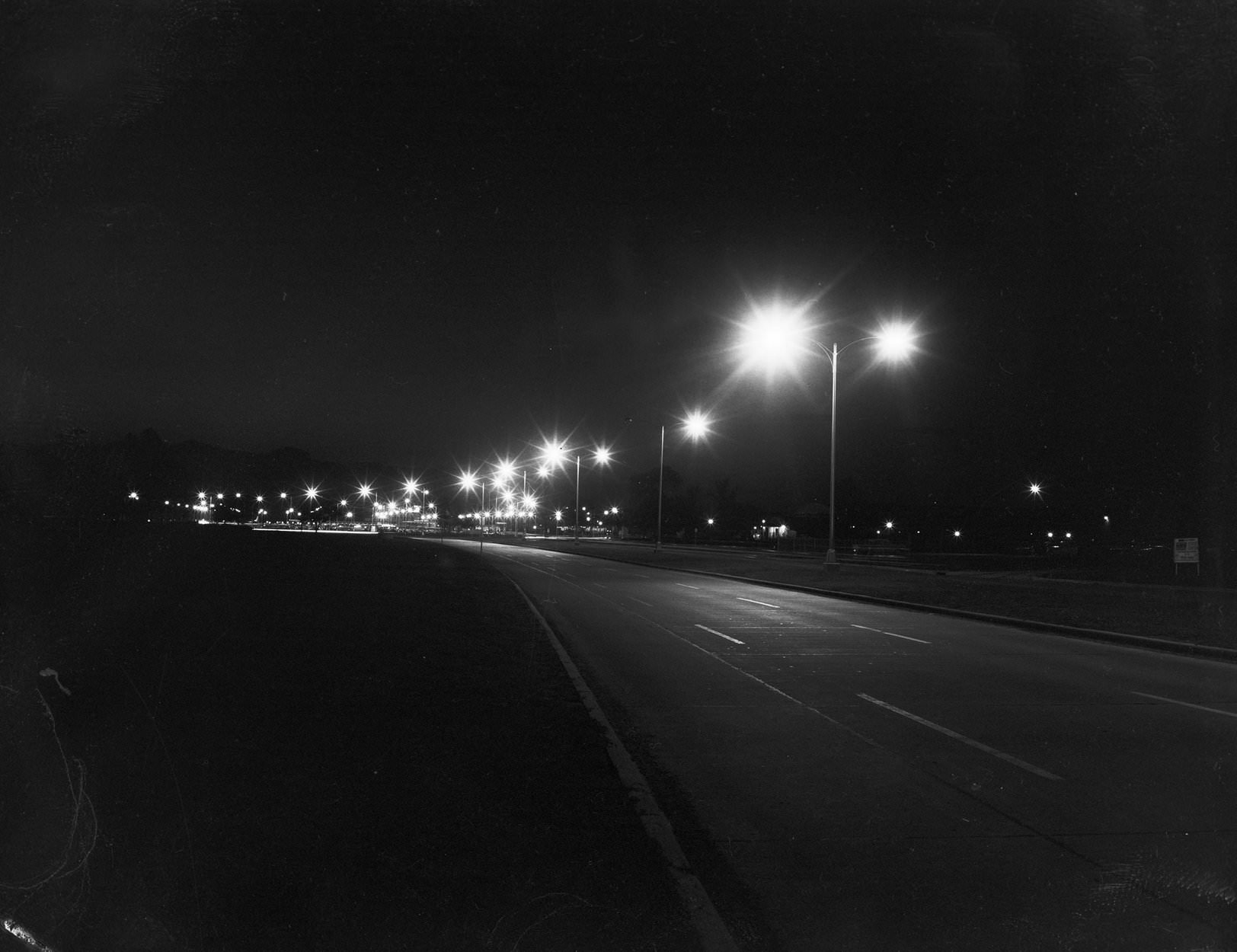 Dallas Love Field at night, 1950. There are lampposts with the lights on, on the side of the street